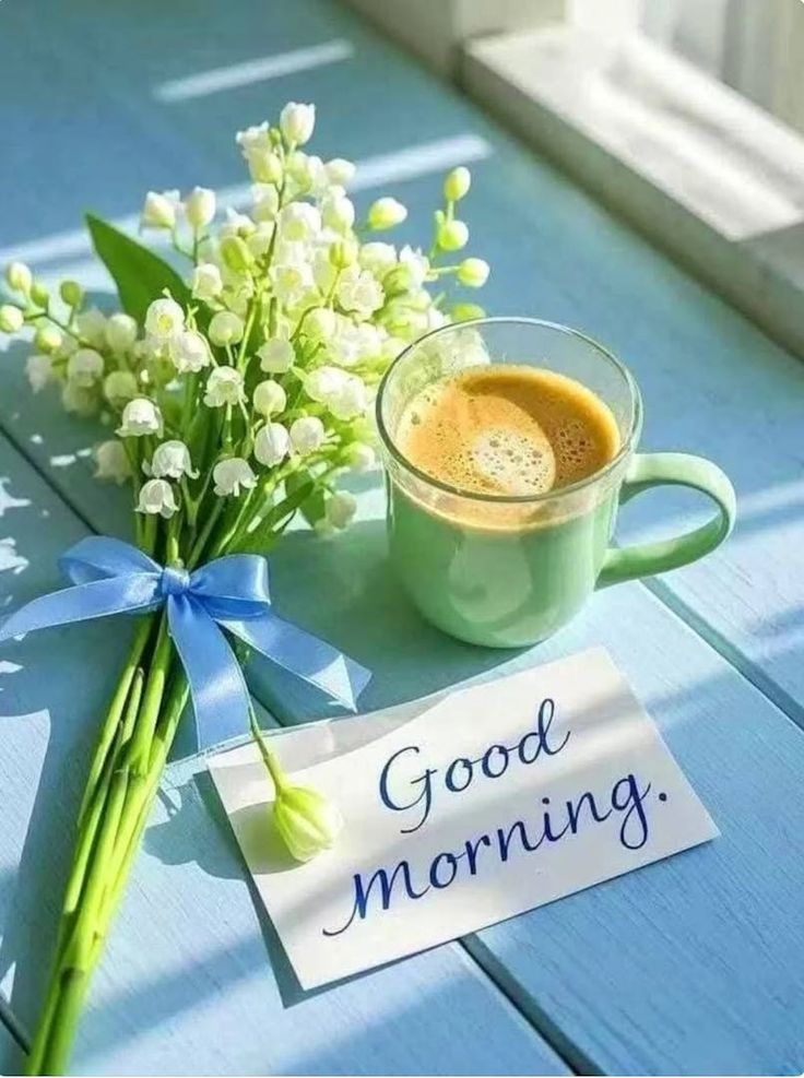 This may contain a cup of coffee next to a bouquet of flowers and a sign that says good morning